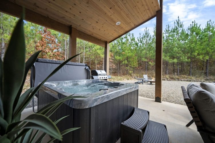 Hot tub on the covered concrete patio with the grill and gravel lot behind it