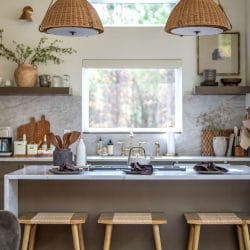 Kitchen island with three wood stools, rattan pendant lights and a window over the sink
