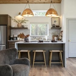 Kitchen with stainless refrigerator, island stools and a gray armchair in the foreground