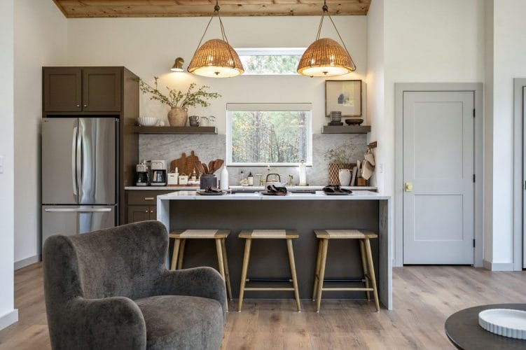 Kitchen with stainless refrigerator, island stools and a gray armchair in the foreground
