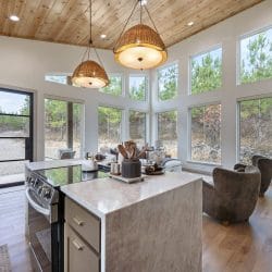 Stone-topped island and electric range, tall windows and a glass door beyond