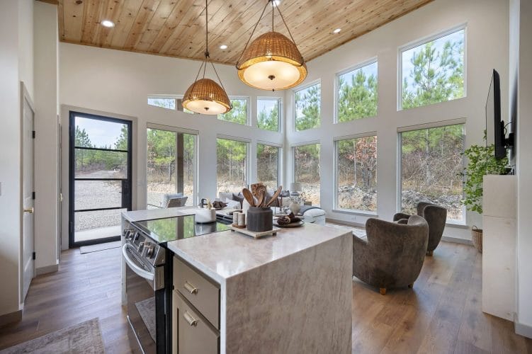 Stone-topped island and electric range, tall windows and a glass door beyond