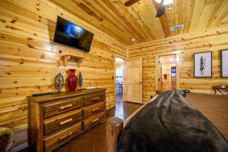 Dresser and TV in the log-bed bedroom, hallway door open at the back