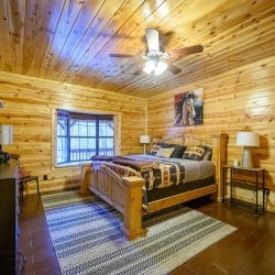 Bed with a wooden headboard and southwestern bedding, horse painting on the wall, ceiling fan above