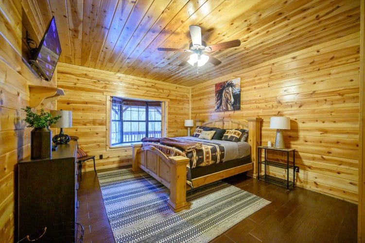 Bed with a wooden headboard and southwestern bedding, horse painting on the wall, ceiling fan above