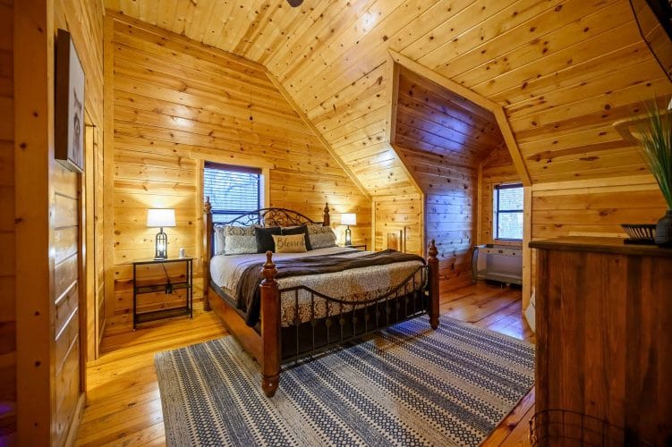 Upstairs bedroom with a black iron-and-wood bed, striped rug and a sloped ceiling