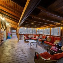 Covered deck with a sofa and chairs with red cushions around a coffee table, string lights overhead