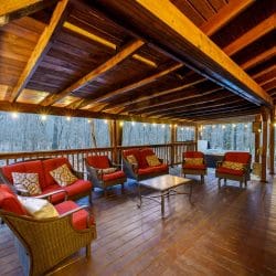 Covered deck with a sectional of red cushions and rocking chairs looking out to the woods