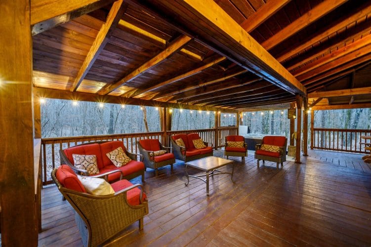 Covered deck with a sectional of red cushions and rocking chairs looking out to the woods