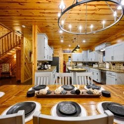 Dining table set with black plates and a ring chandelier, kitchen behind