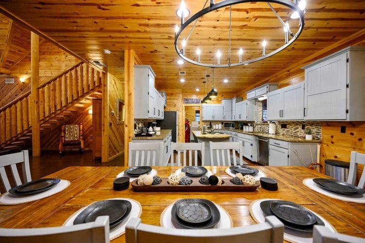 Dining table set with black plates and a ring chandelier, kitchen behind