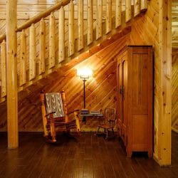 Staircase with a log railing, a rocking chair and a wooden armoire beneath it