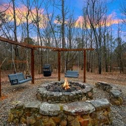 Stone fire pit with a flame and bench swings hanging from a timber frame