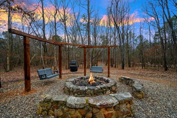 Stone fire pit with a flame and bench swings hanging from a timber frame