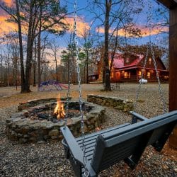 Fire pit with a bench swing in the foreground and the cabin behind it