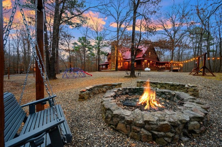 Burning stone fire pit with the play dome and cabin behind