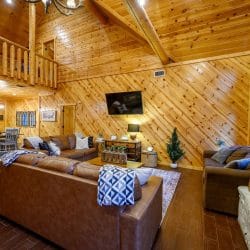 Great room with leather sofas, a TV and a loft railing above under a high pine ceiling