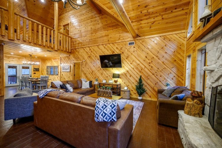Great room with leather sofas, a TV and a loft railing above under a high pine ceiling