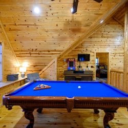 Loft with a blue-felt pool table under a sloped knotty pine ceiling
