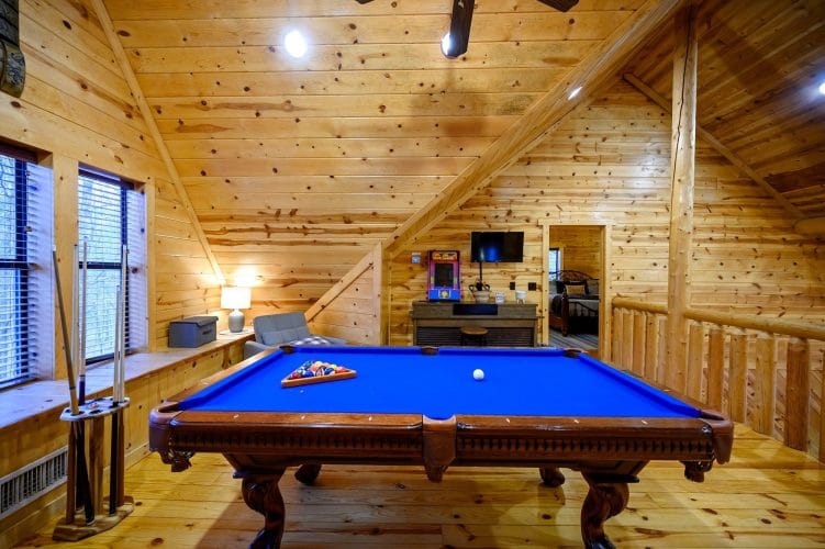 Loft with a blue-felt pool table under a sloped knotty pine ceiling