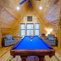 Pool table with two gray chairs in front of three windows under the pitched ceiling
