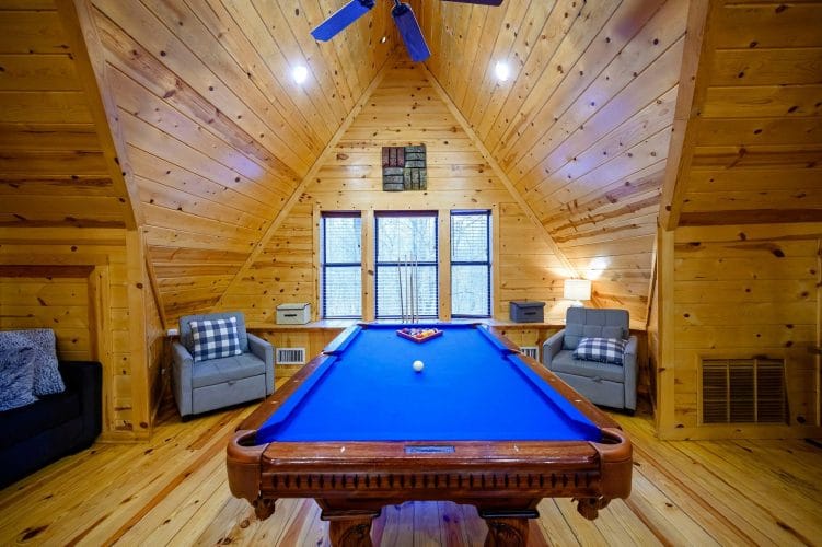 Pool table with two gray chairs in front of three windows under the pitched ceiling