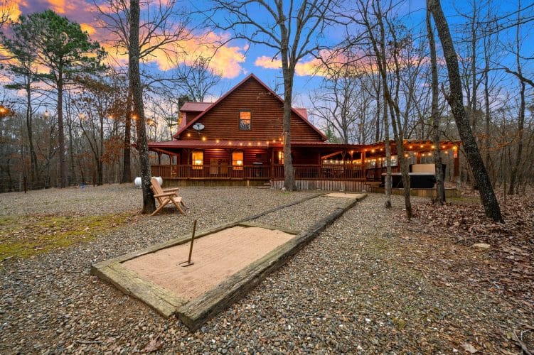Horseshoe pit in the gravel yard with the cabin's lit porch behind it