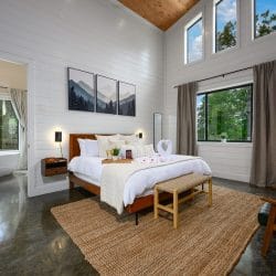 King bed on a woven jute rug with three mountain prints above it, the bathroom visible through a doorway