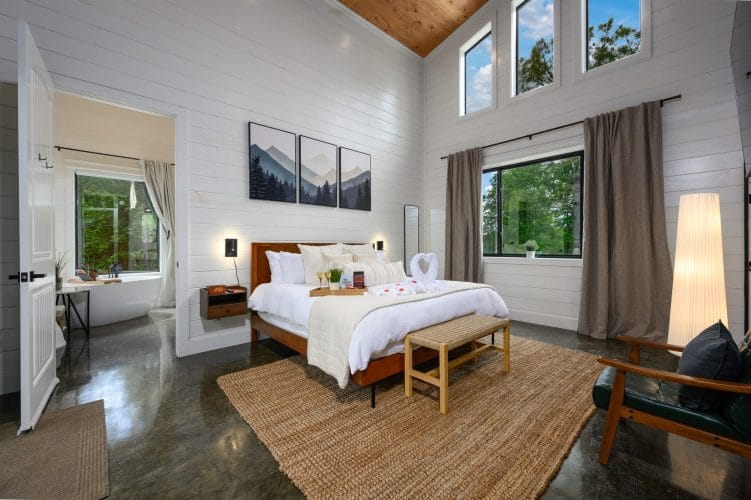 King bed on a woven jute rug with three mountain prints above it, the bathroom visible through a doorway