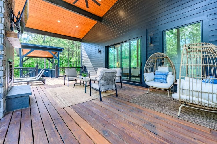 Covered deck with a sofa, two wicker egg chairs and sliding glass doors
