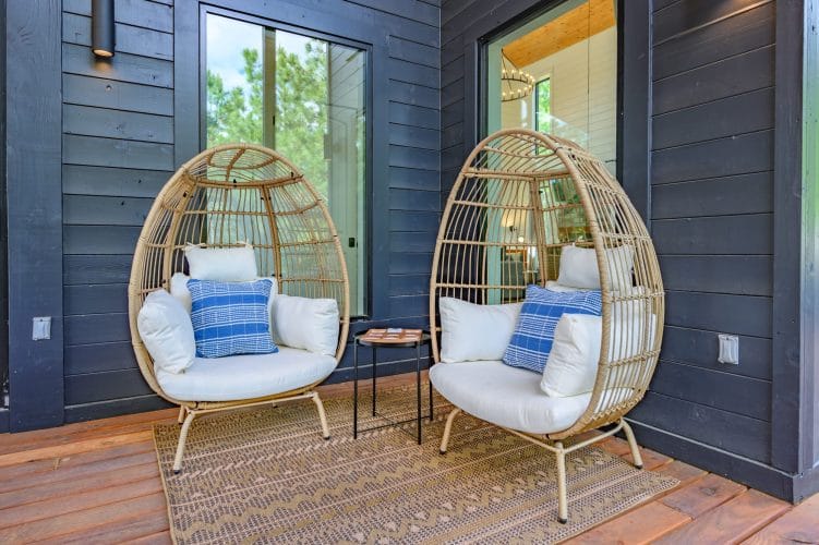 Two wicker egg chairs on the deck beside dark siding