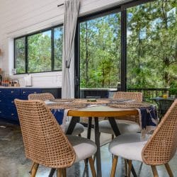 Round dining table with rattan chairs beside floor-to-ceiling glass doors