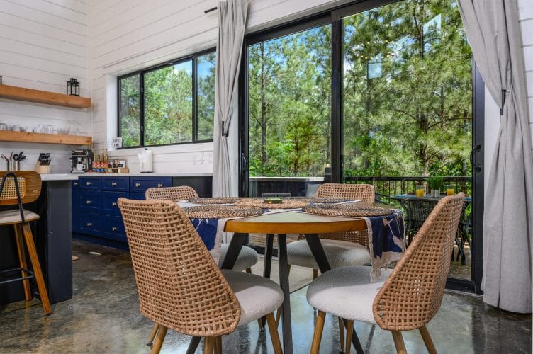 Round dining table with rattan chairs beside floor-to-ceiling glass doors