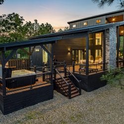 Back of the cabin with a covered deck, the hot tub platform and string lights at dusk