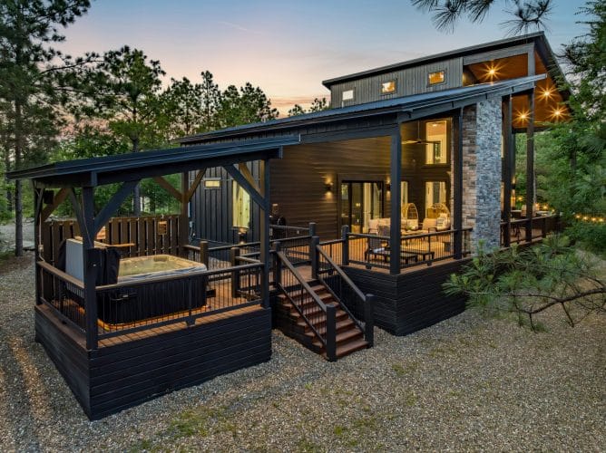 Back of the cabin with a covered deck, the hot tub platform and string lights at dusk