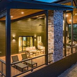 Side of the cabin with stone pillars and a covered deck lit at dusk