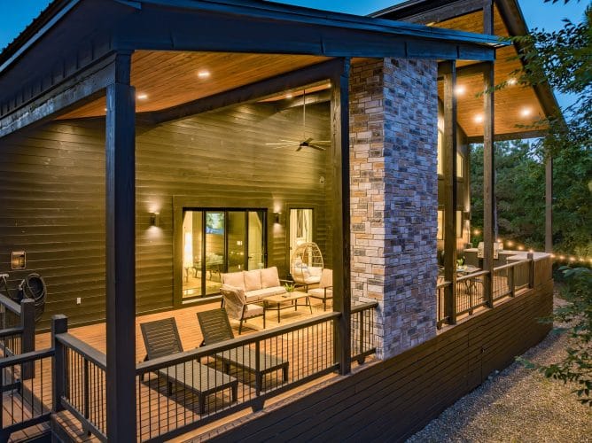 Side of the cabin with stone pillars and a covered deck lit at dusk