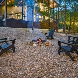 Fire pit with black Adirondack chairs on gravel and the lit deck behind