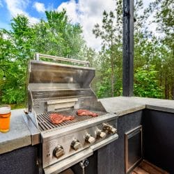 Built-in grill with steaks on it and a beer on the concrete counter