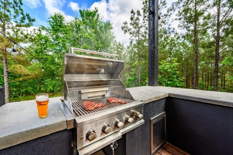 Built-in grill with steaks on it and a beer on the concrete counter