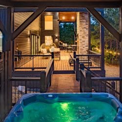 Raised walkway leading to a lit hot tub, seen from the covered porch at dusk