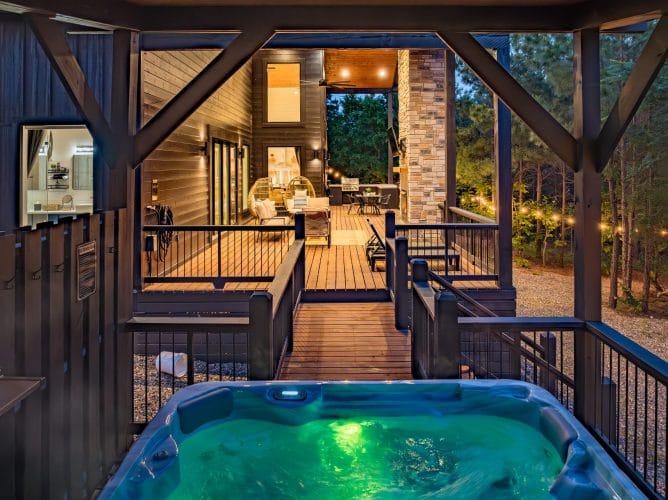 Raised walkway leading to a lit hot tub, seen from the covered porch at dusk