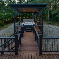 Hot tub under its own pergola at the end of a raised walkway with string lights