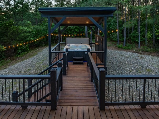 Hot tub under its own pergola at the end of a raised walkway with string lights