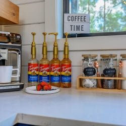 Espresso machine with flavored syrup bottles and canisters on a white counter, with a Coffee Time sign