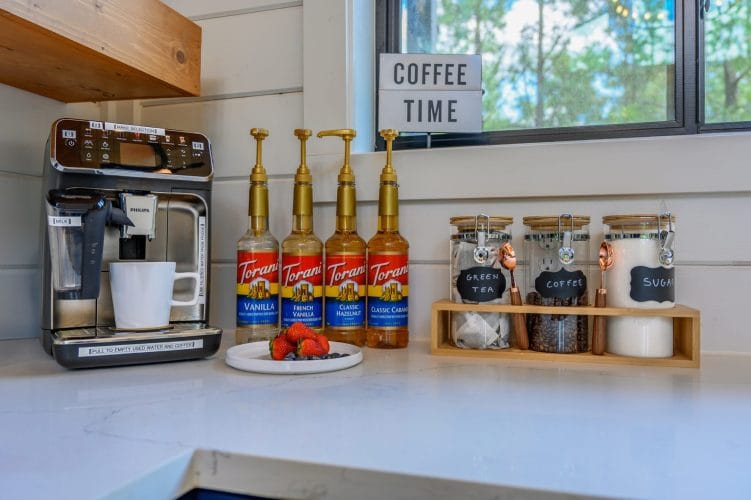 Espresso machine with flavored syrup bottles and canisters on a white counter, with a Coffee Time sign