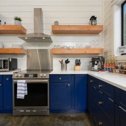 Kitchen with navy cabinets, open wood shelves and a stainless range