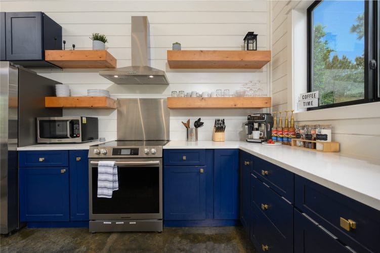 Kitchen with navy cabinets, open wood shelves and a stainless range