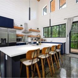 Kitchen with a white island, tall rattan-back stools and a wall of windows