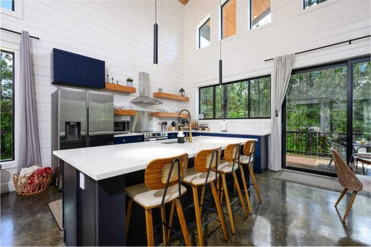 Kitchen with a white island, tall rattan-back stools and a wall of windows